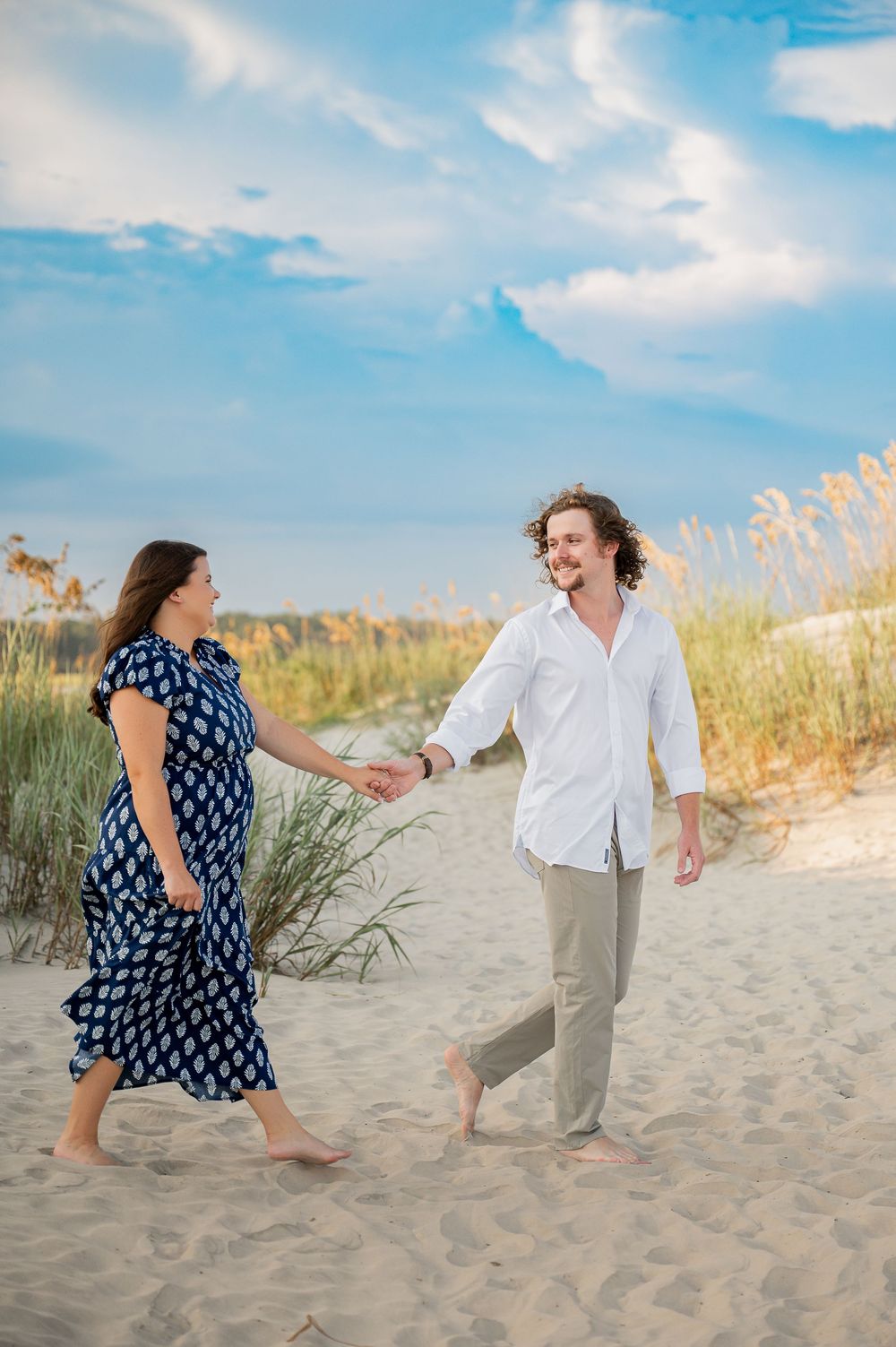 A couple plays and dances together on sandy beach dunes during a sunny afternoon.