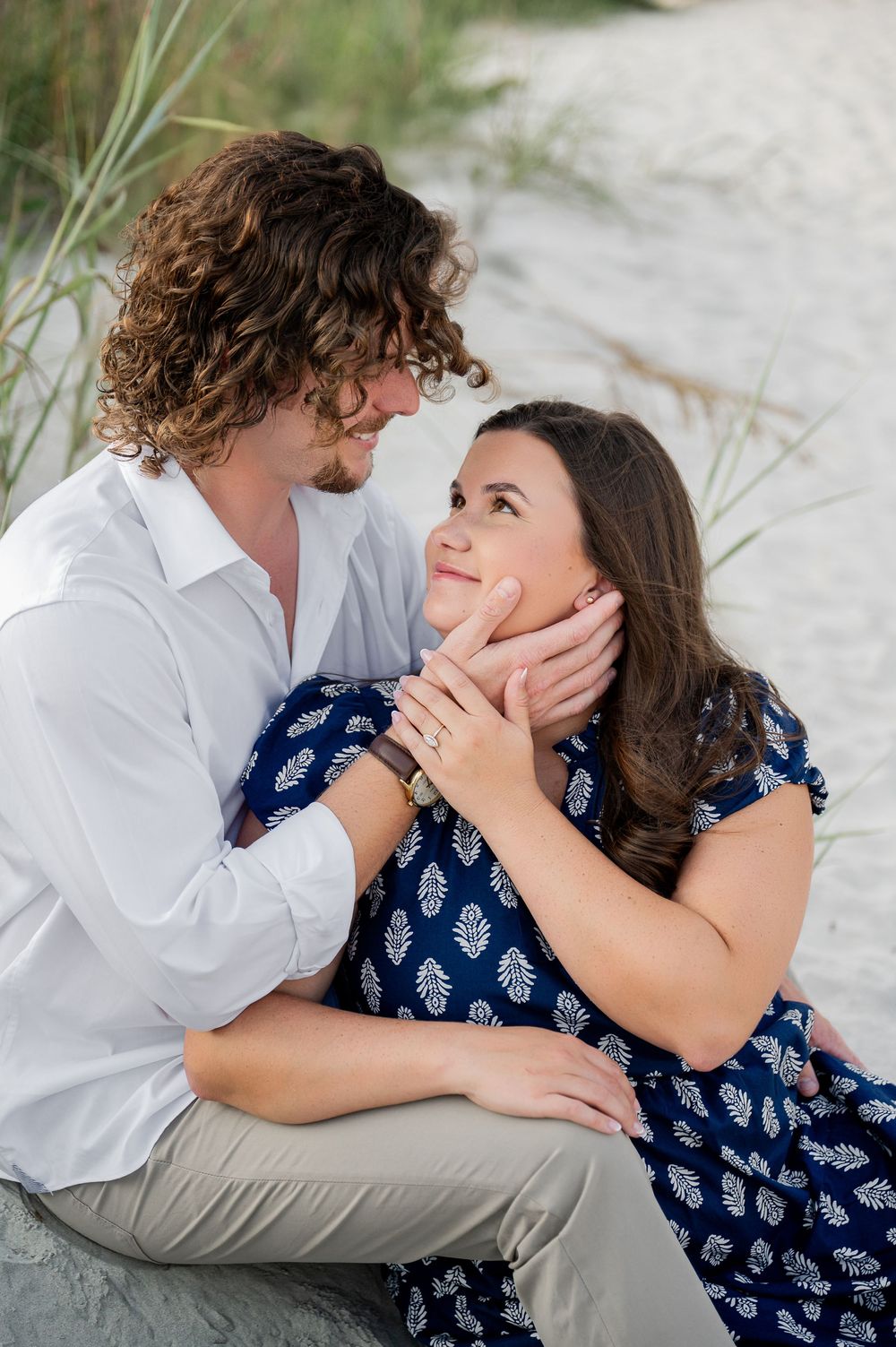 Romantic couple sharing intimate moments on a sandy beach with sea grass in the background.