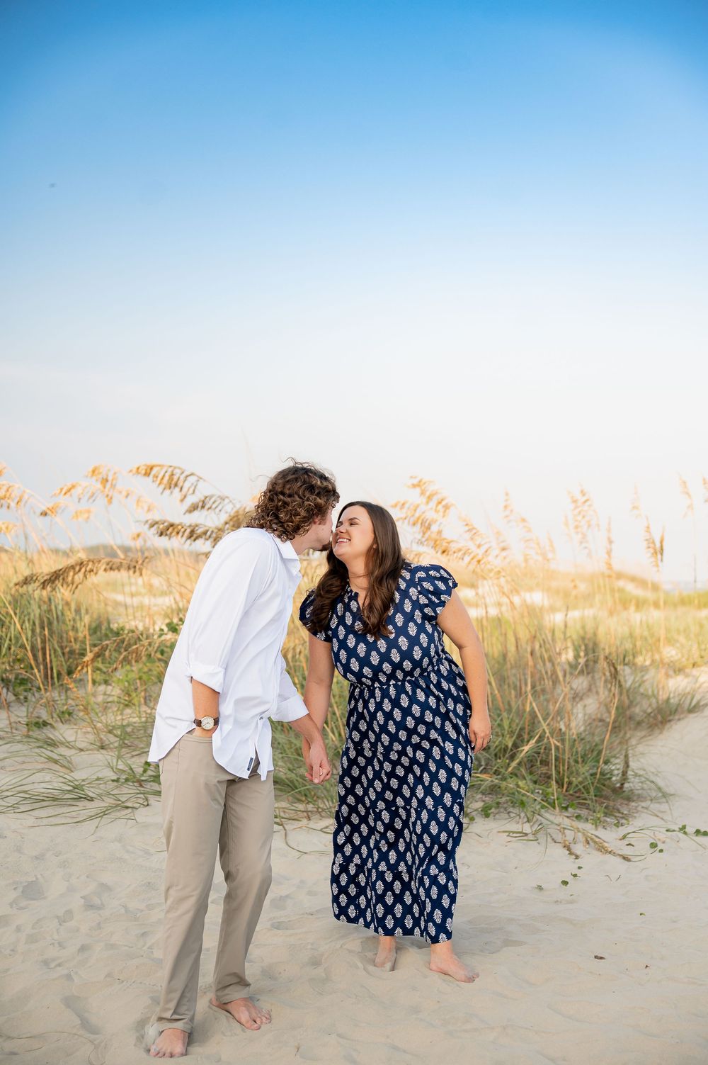 Couple in coordinated outfits playfully interacting on coastal sand dunes.