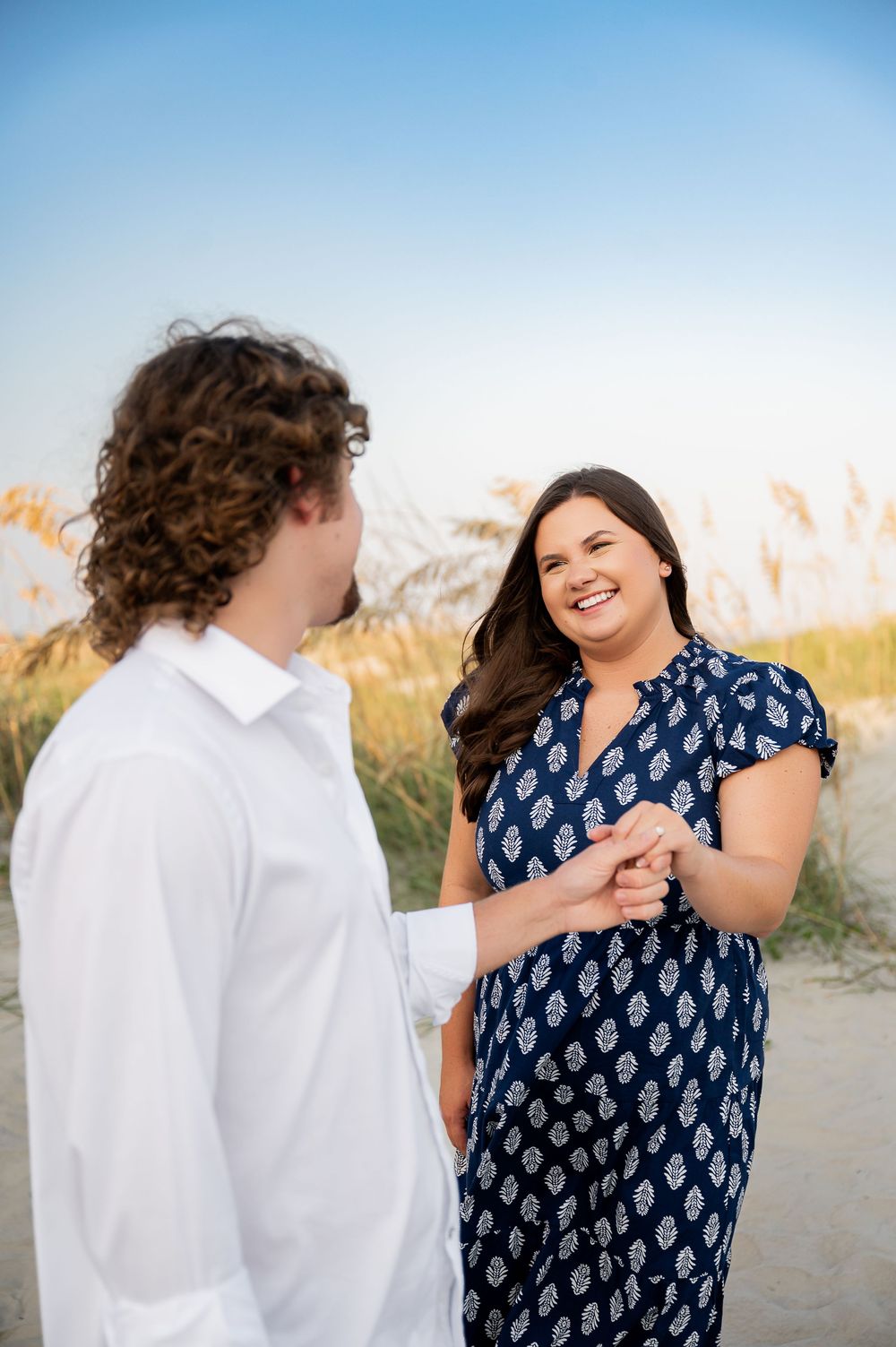 Joyful couple sharing laughter during their beach photoshoot against blue sky.