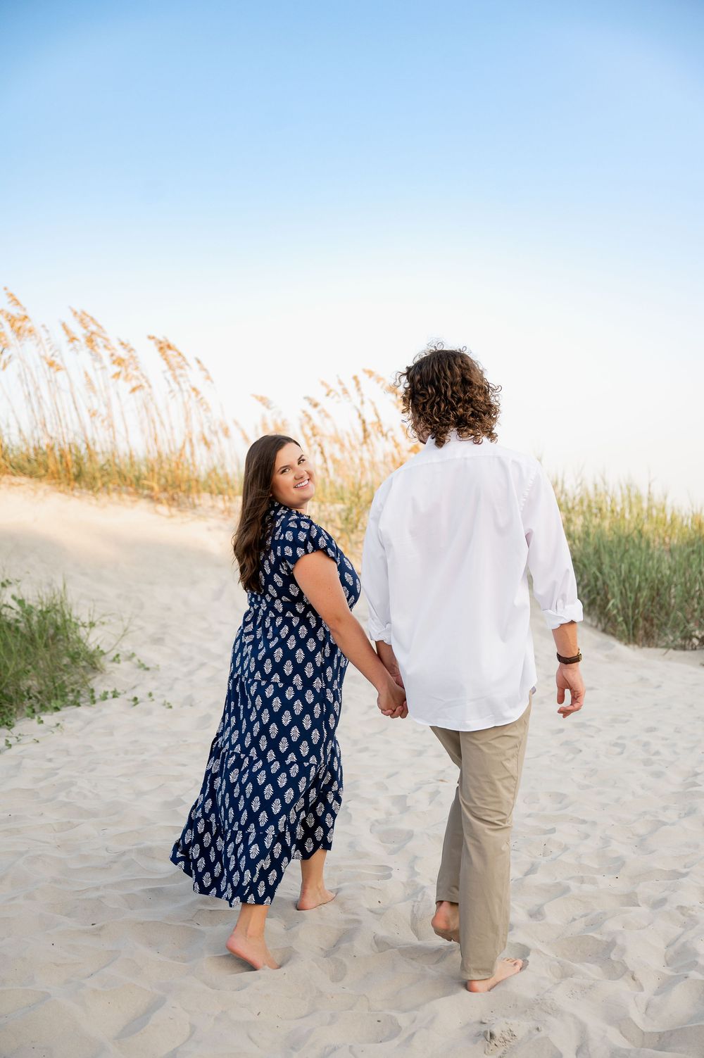 Couple in navy and white outfits walking together on sandy beach path.