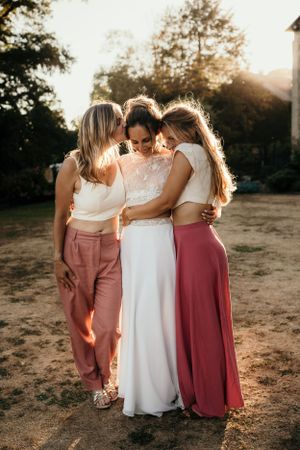 Three friends share an intimate group hug during sunset wedding celebration.
