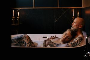 Couple sharing intimate candlelit moment in bathtub with visible tattoos.
