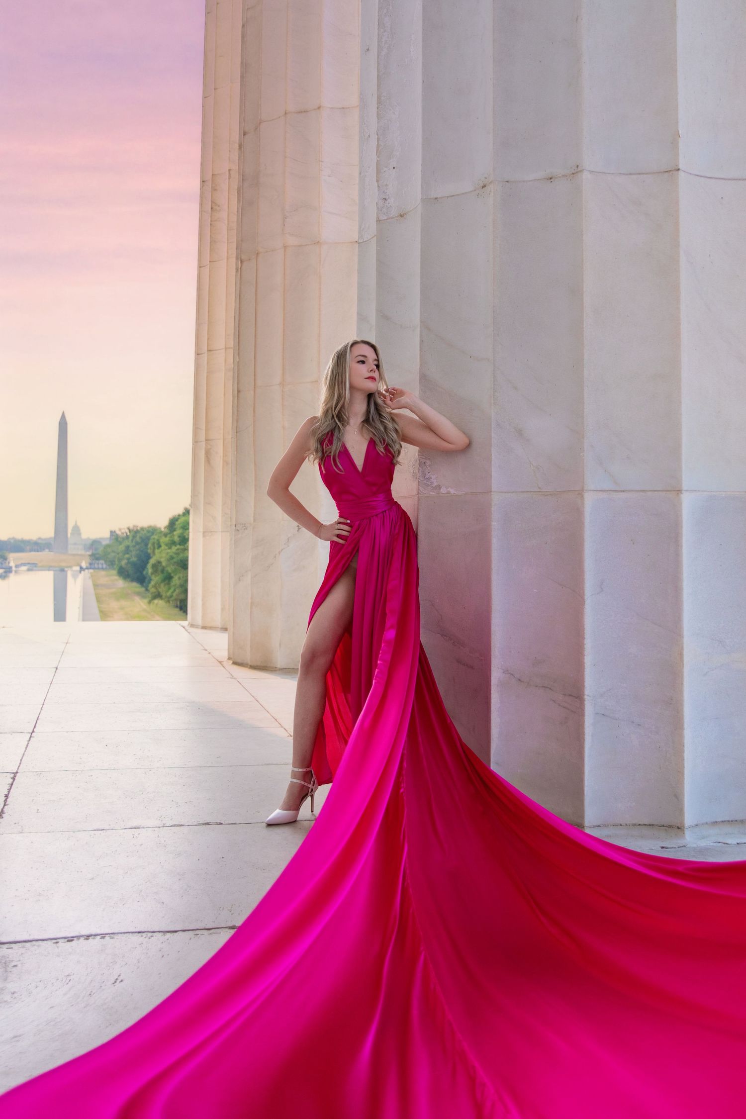 A flowing hot pink gown with dramatic train creates an elegant silhouette against white marble columns at sunset. Flying Dress Photoshoot