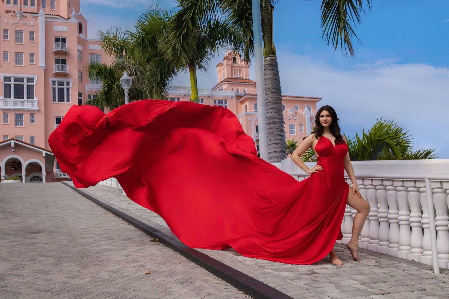 Bright pink flowing fabric dress creates dramatic movement between classical white columns at sunset.