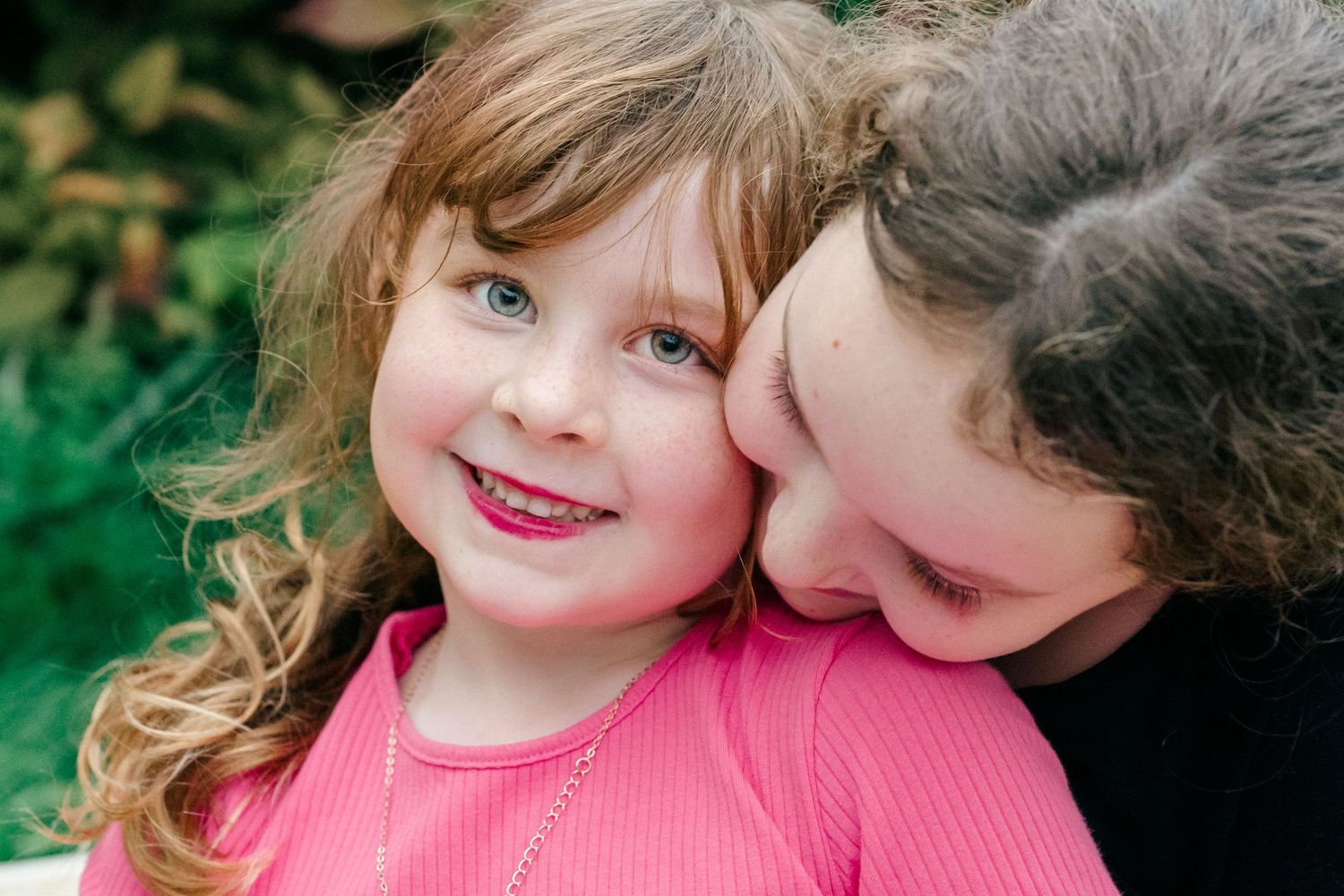 Natural family photography of two sisters cuddling closely together during an unposed outdoor family photoshoot