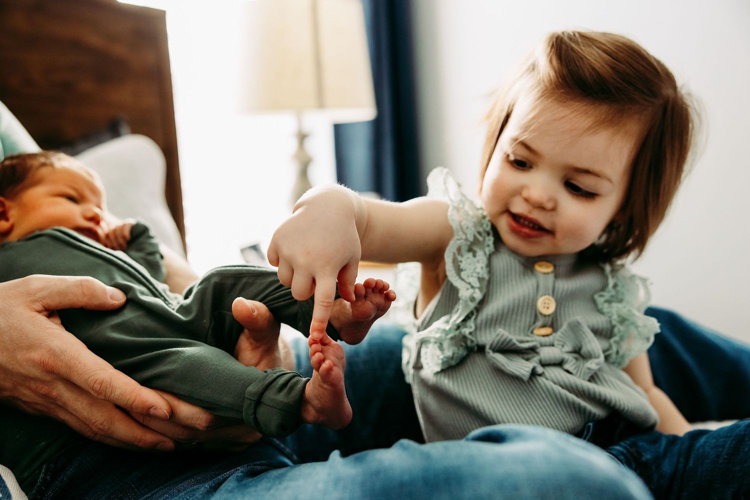 Older sibling gently interacting with newborn baby during a lifestyle newborn photography session at home