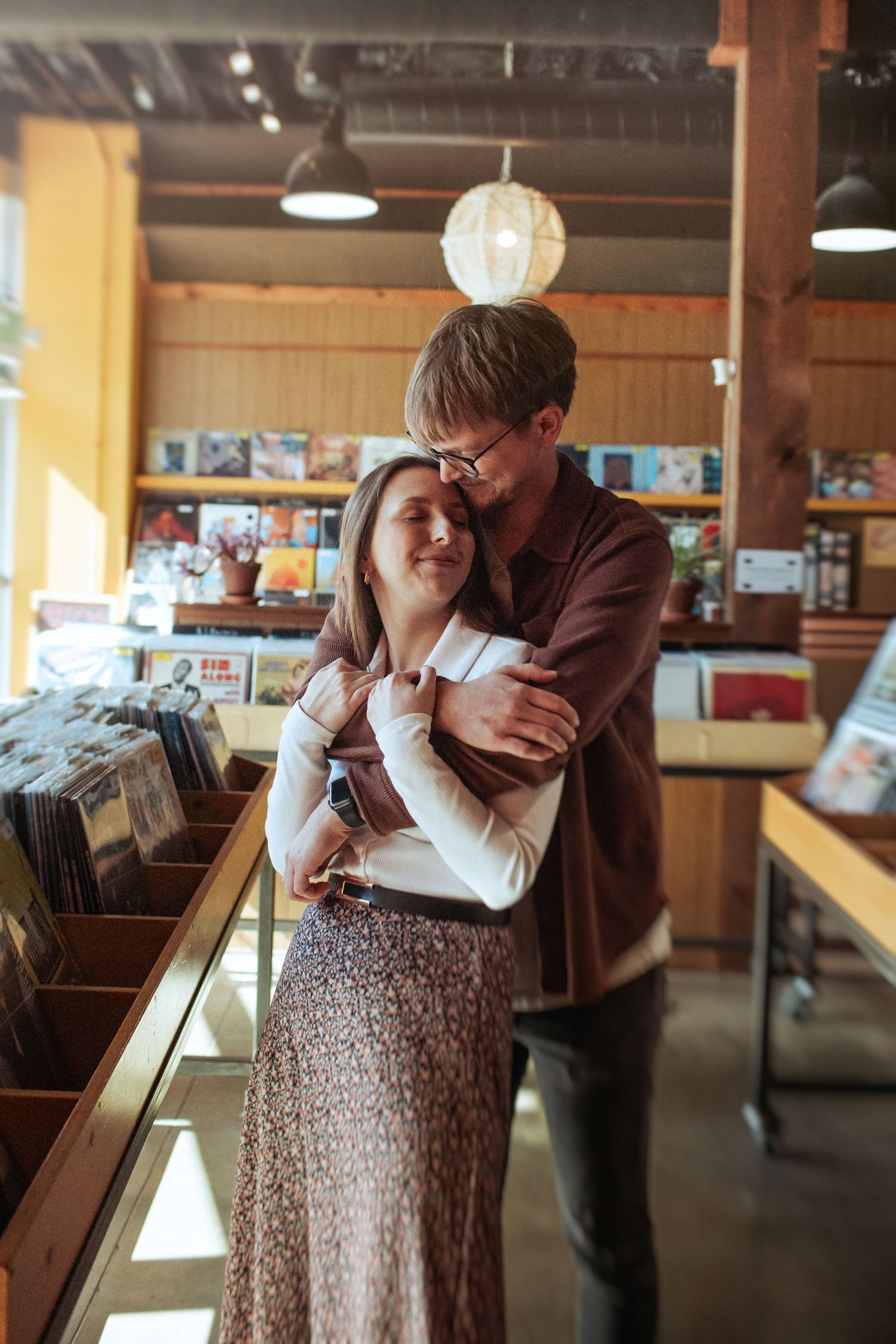 A romantic moment between a couple in a record store with wooden shelves and soft lighting. Indianapolis, Indiana engagement session.