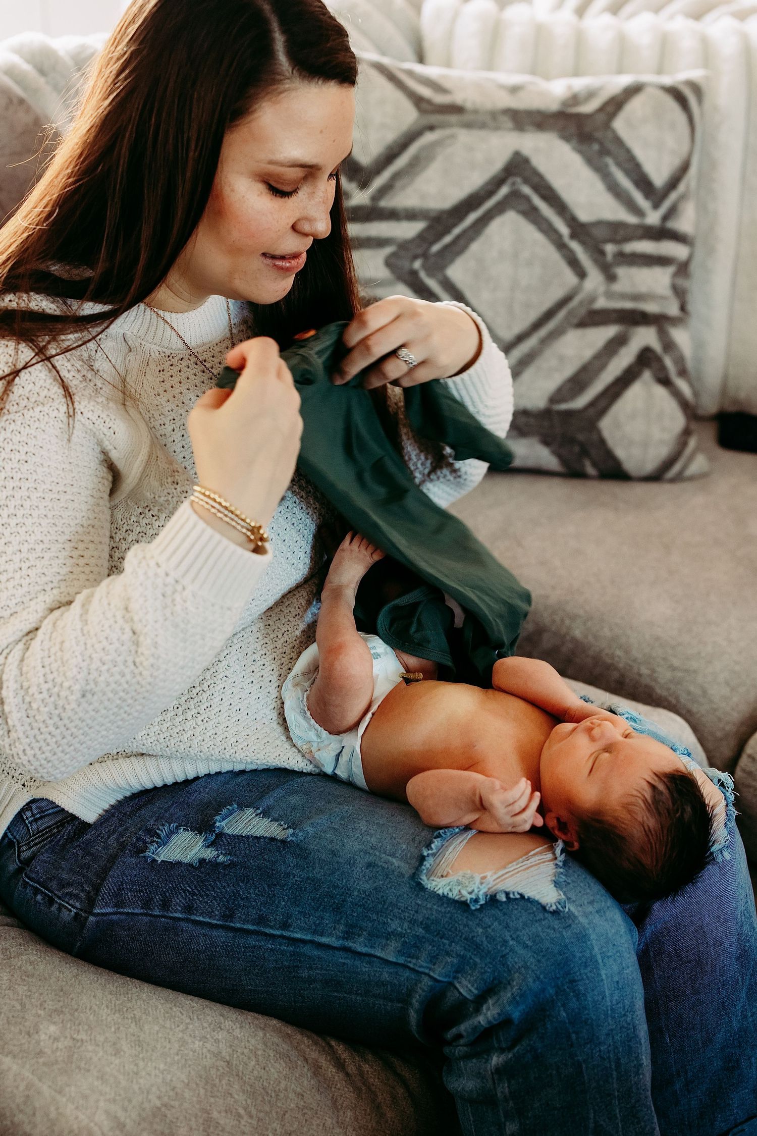 A young child in a blue dress reaches out to touch a baby lying on a floral blanket in soft natural lighting.
