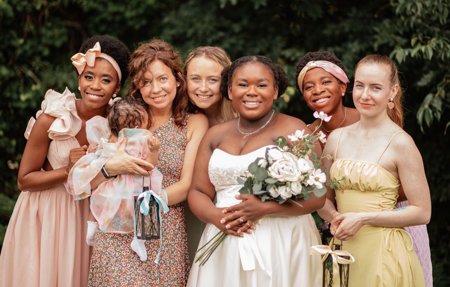 A joyful wedding party poses together wearing pastel dresses in varying styles.