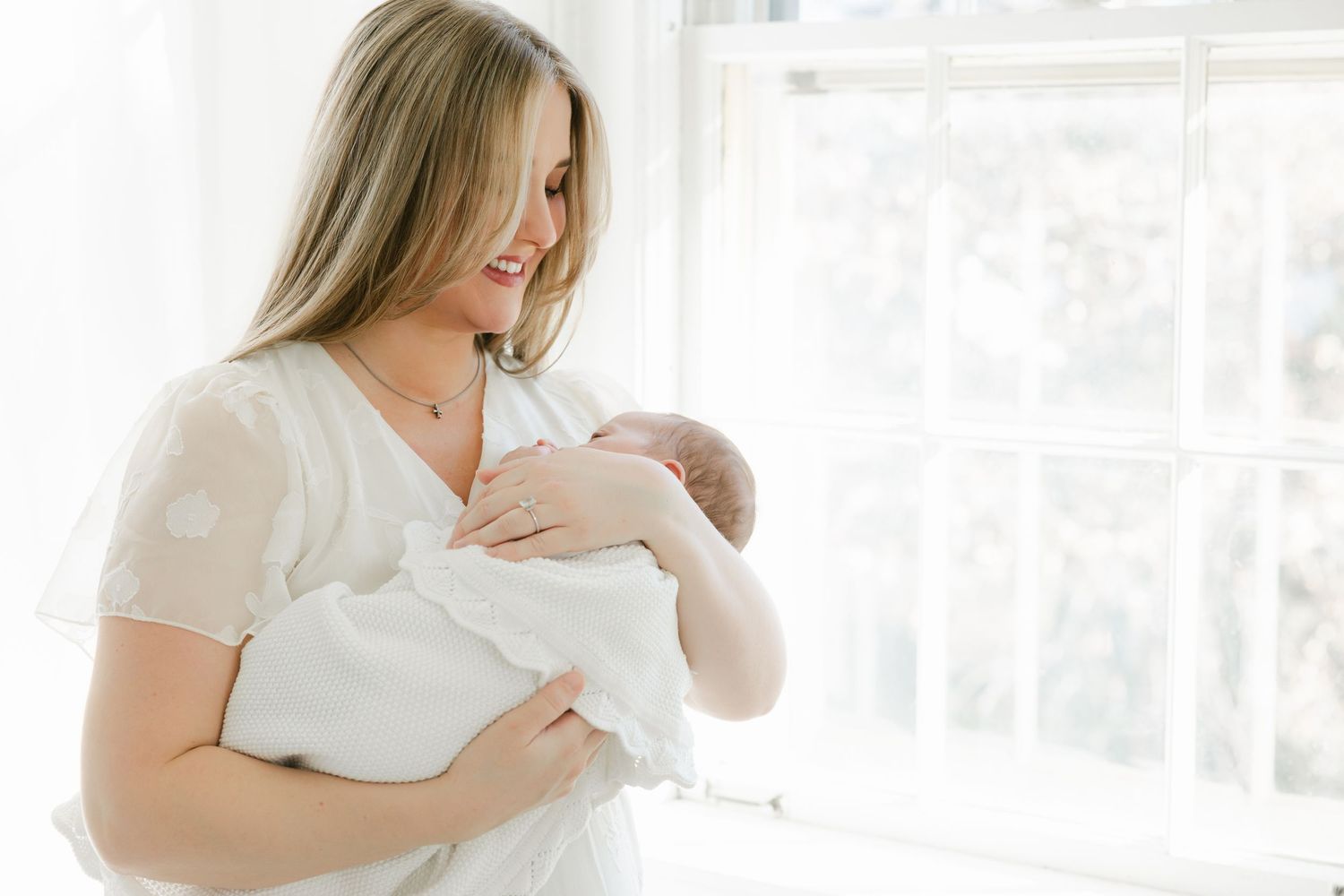 A person in white clothing holds a baby against their chest in a bright sunlit room.