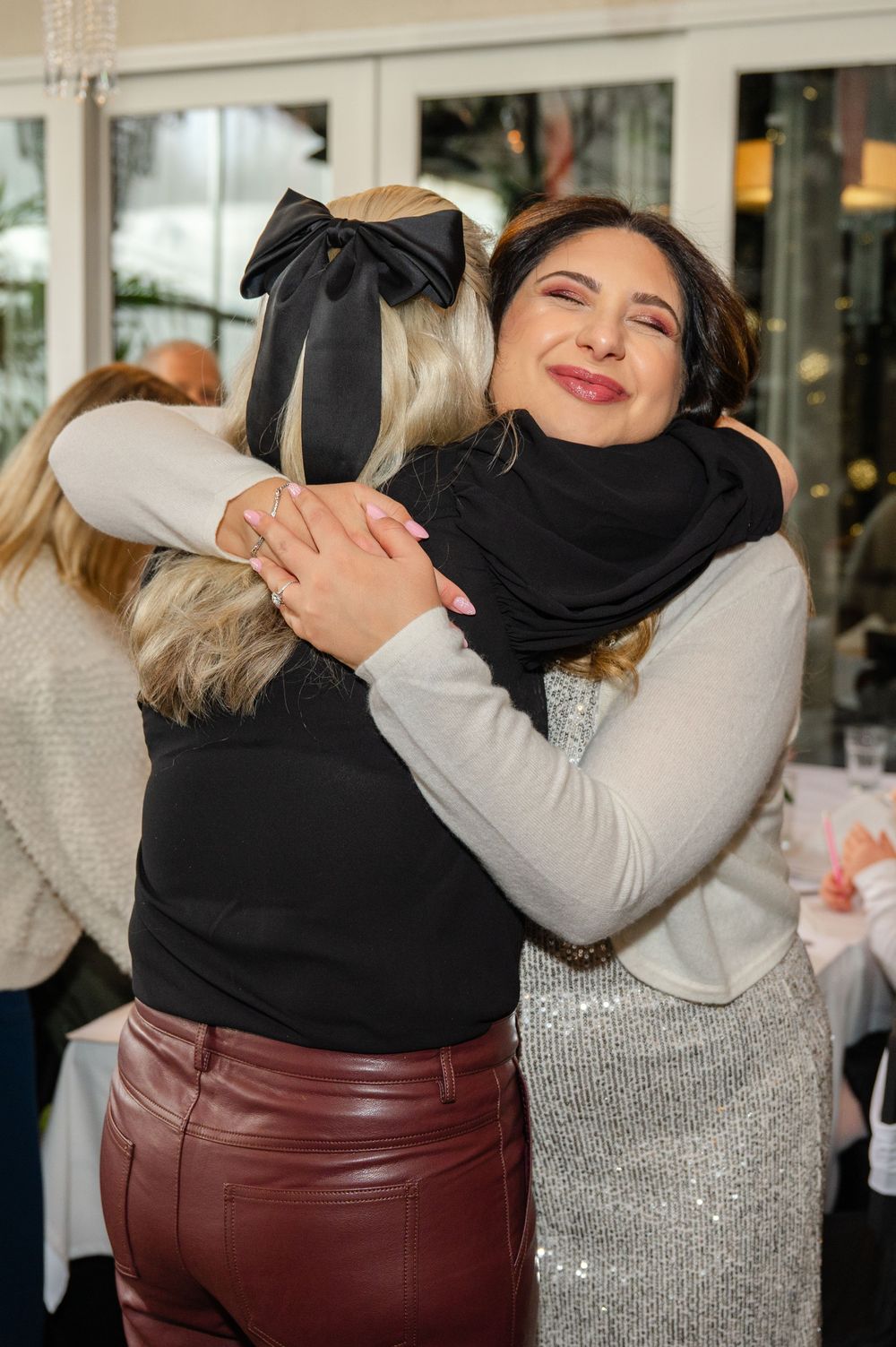 Two friends share a warm embrace wearing contrasting black and silver outfits at a social gathering.