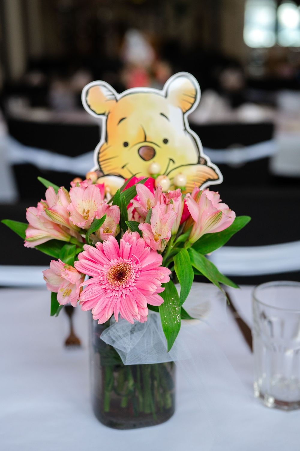 Pink gerbera daisies and greenery arranged in small glass vases with a decorative teddy bear accent.