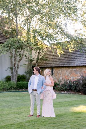 A couple walks together on a lush green lawn beside a garden wall during a sunny afternoon.