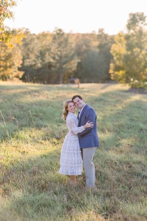 A couple embraces in a sun-drenched field during golden hour as autumn colors paint the landscape behind them.