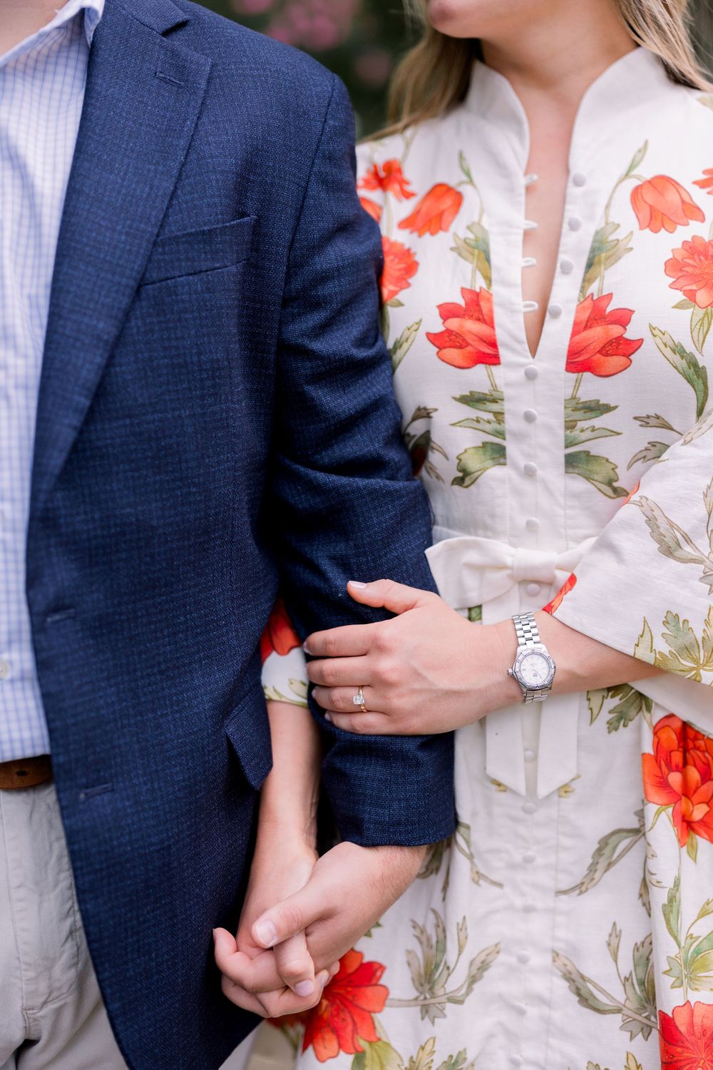 Close-up of couple in wedding attire with navy suit and white floral dress with orange poppy print.