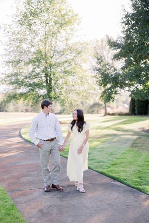 A couple walking together on a paved path surrounded by lush green grass and trees on a sunny day.