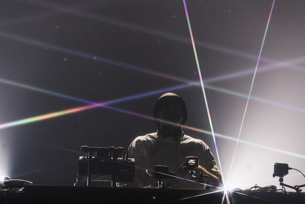 DJ performs on stage with dramatic lighting effects and beams creating a spectacular visual atmosphere at a concert.
