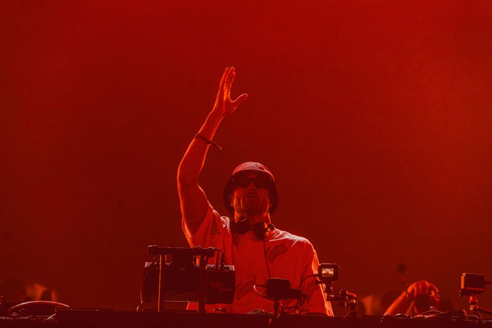 Musicians perform on stage bathed in dramatic red lighting during a live concert performance.