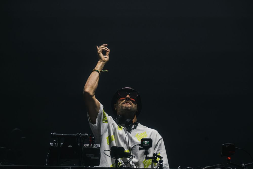 A DJ performs at a dark nightclub with dramatic lighting and equipment visible in the background.