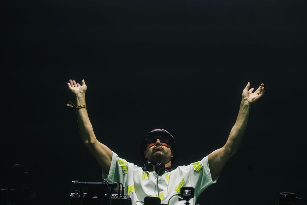 Performers on stage raise their arms triumphantly during a concert performance in a dark venue.