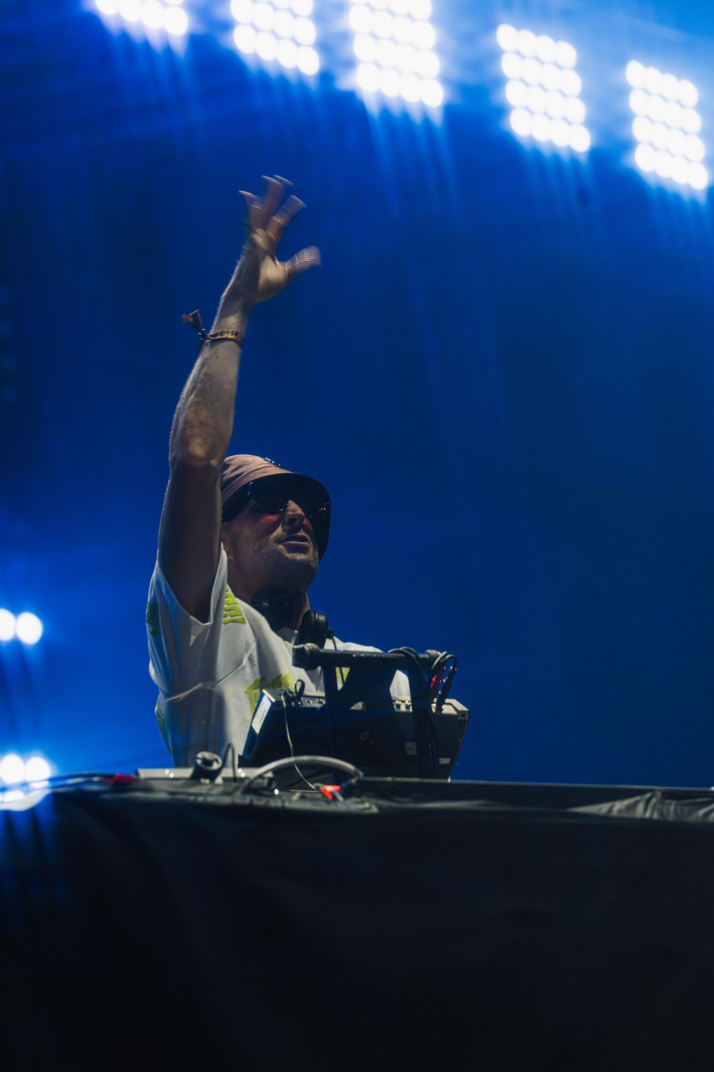 DJ performs energetically behind turntables on stage with dramatic blue lighting and raised hands.