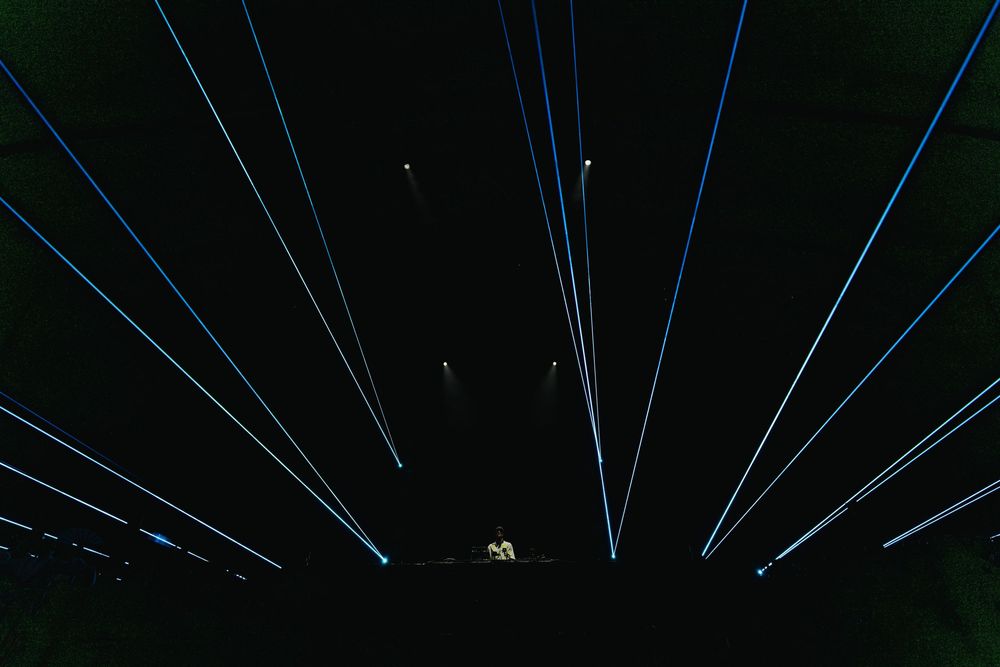 Blue laser beams shine through darkness creating dramatic parallel lines against a black background at a nighttime show.