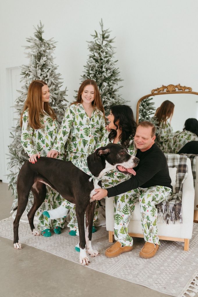 Family and their Great Dane dog create fun poses in matching holiday pajamas by Christmas trees.