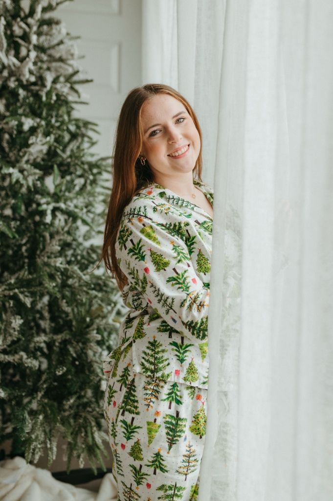 A festive winter scene with someone wearing a cozy botanical print sweater next to a decorated Christmas tree.