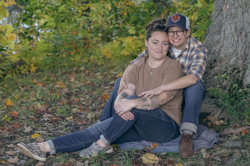 Couple in casual fall attire poses together on fallen leaves during an outdoor autumn photoshoot session.