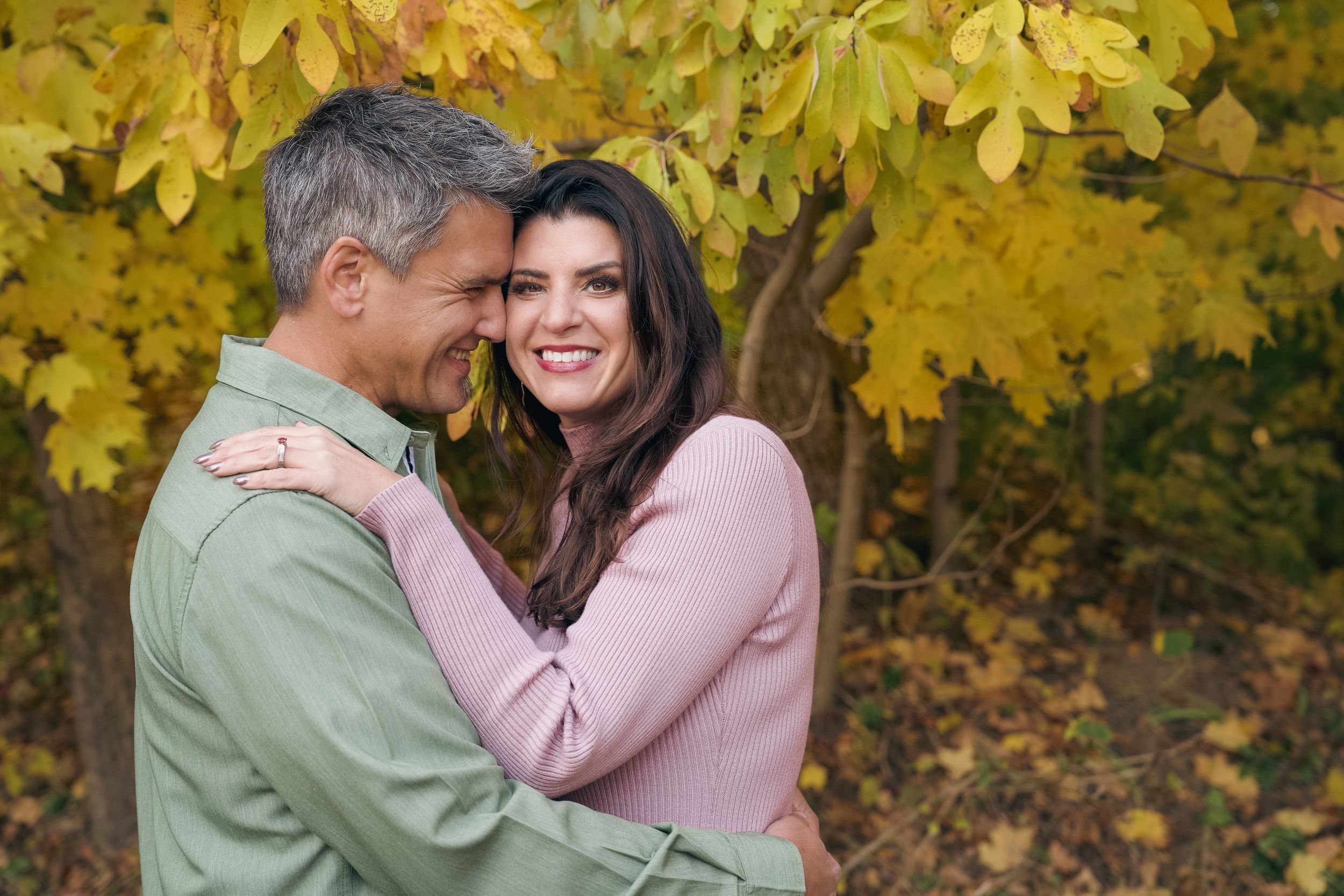 Couple embraces outdoors against vibrant yellow autumn foliage in a romantic fall photoshoot.