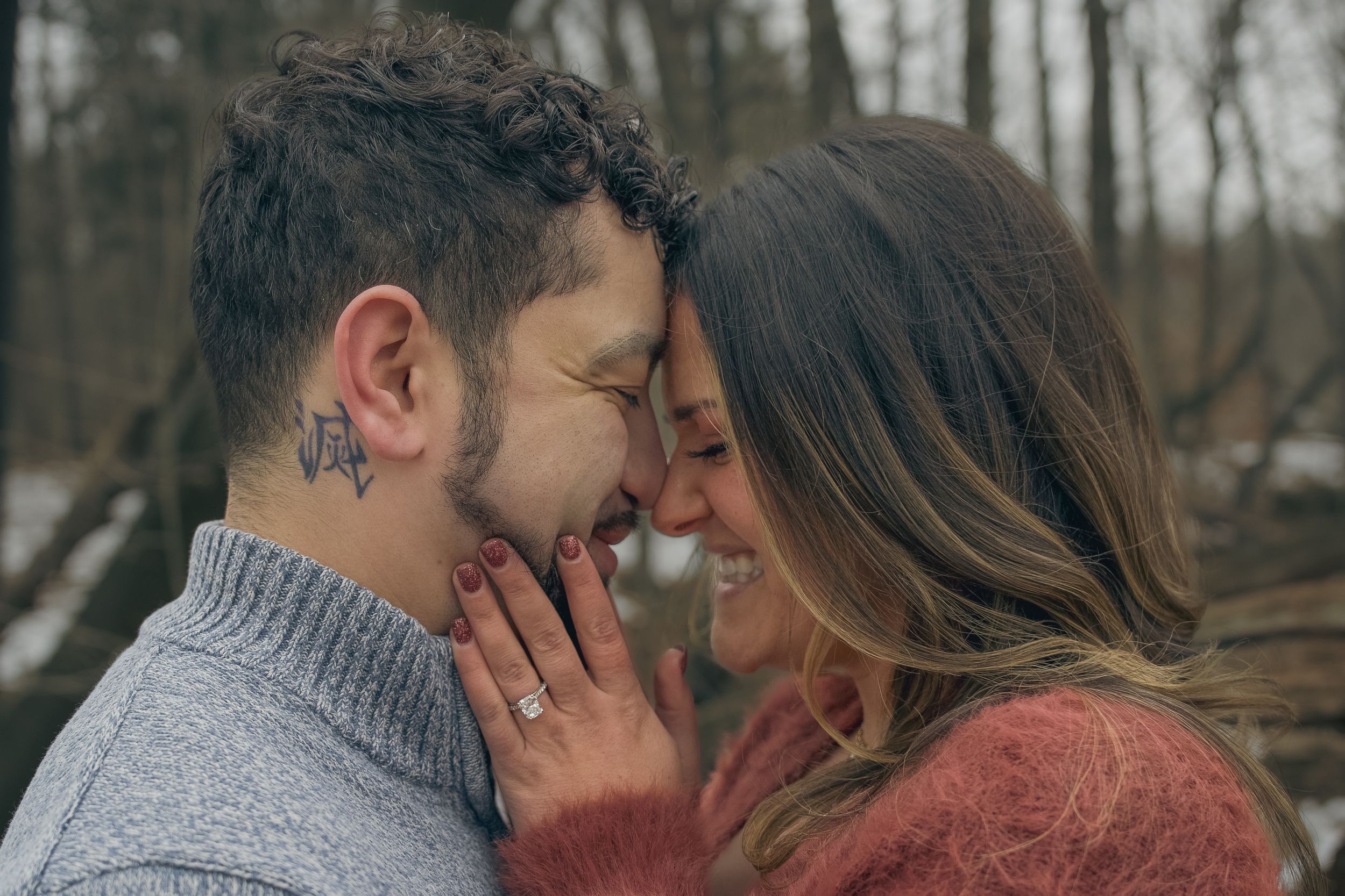 Romantic couple in winter clothing share intimate moments in a forest during a photo session.