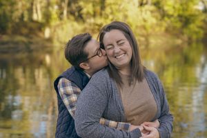 A loving couple shares an intimate moment by a serene lake with autumn trees reflecting in the water.