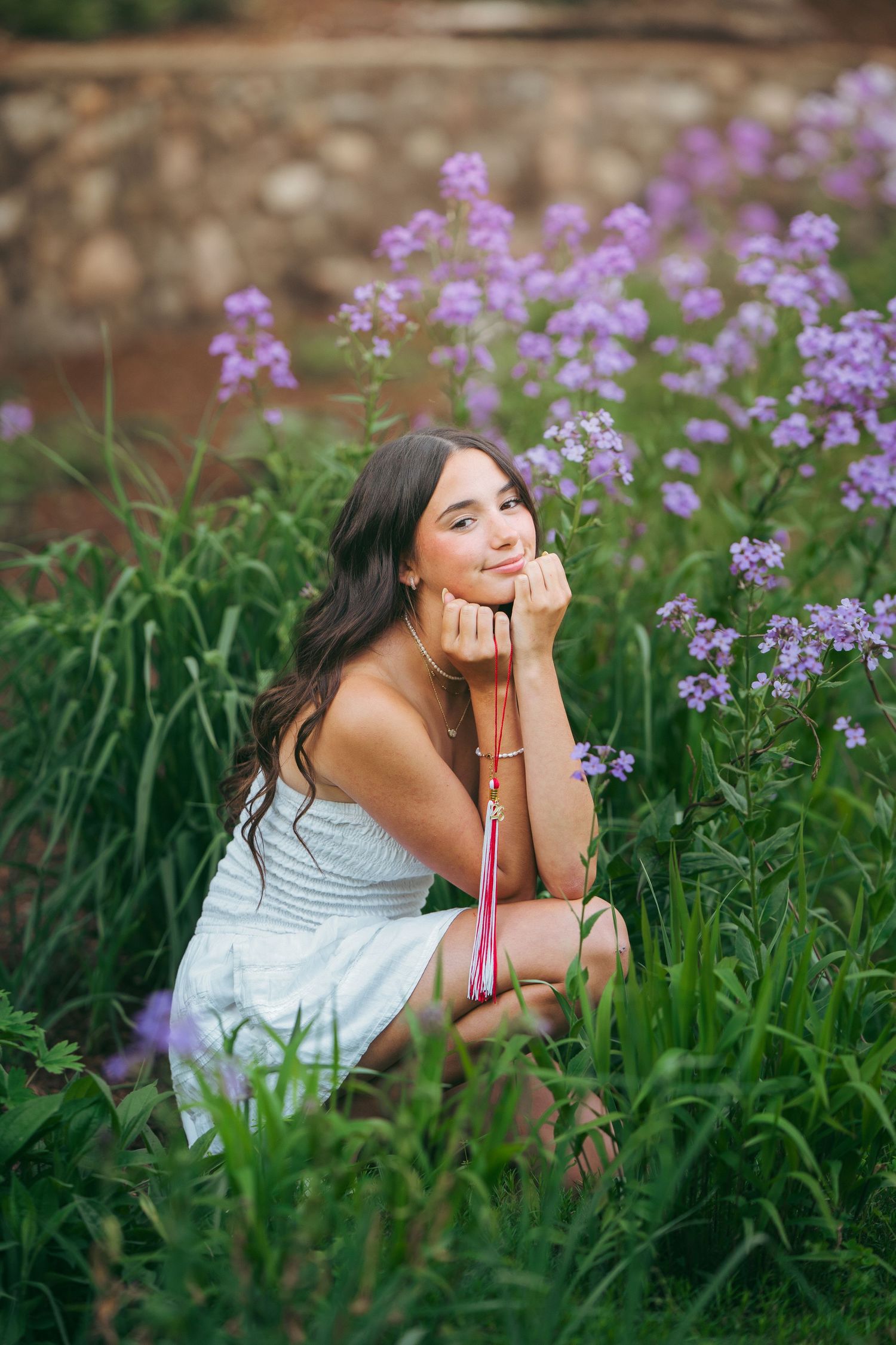 Smiling teen girl in floral dress posing with bright yellow sunflowers in a lush green garden.