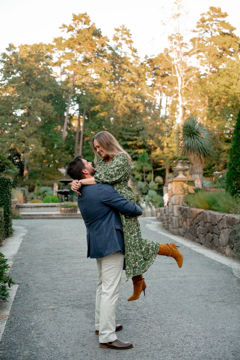 A playful couple dancing and twirling on a garden pathway surrounded by fall foliage.