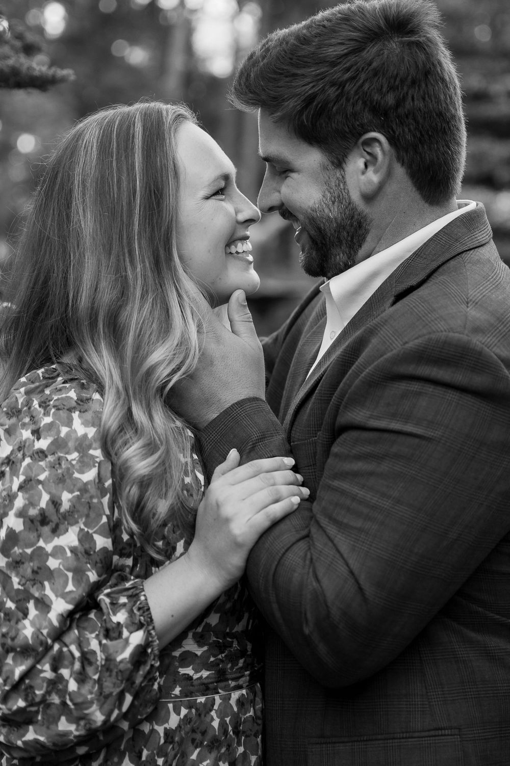An intimate black and white portrait of a couple sharing a tender moment outdoors.