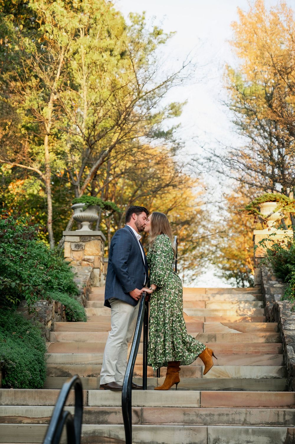 A romantic couple embracing on stone steps in a garden setting with autumn trees.