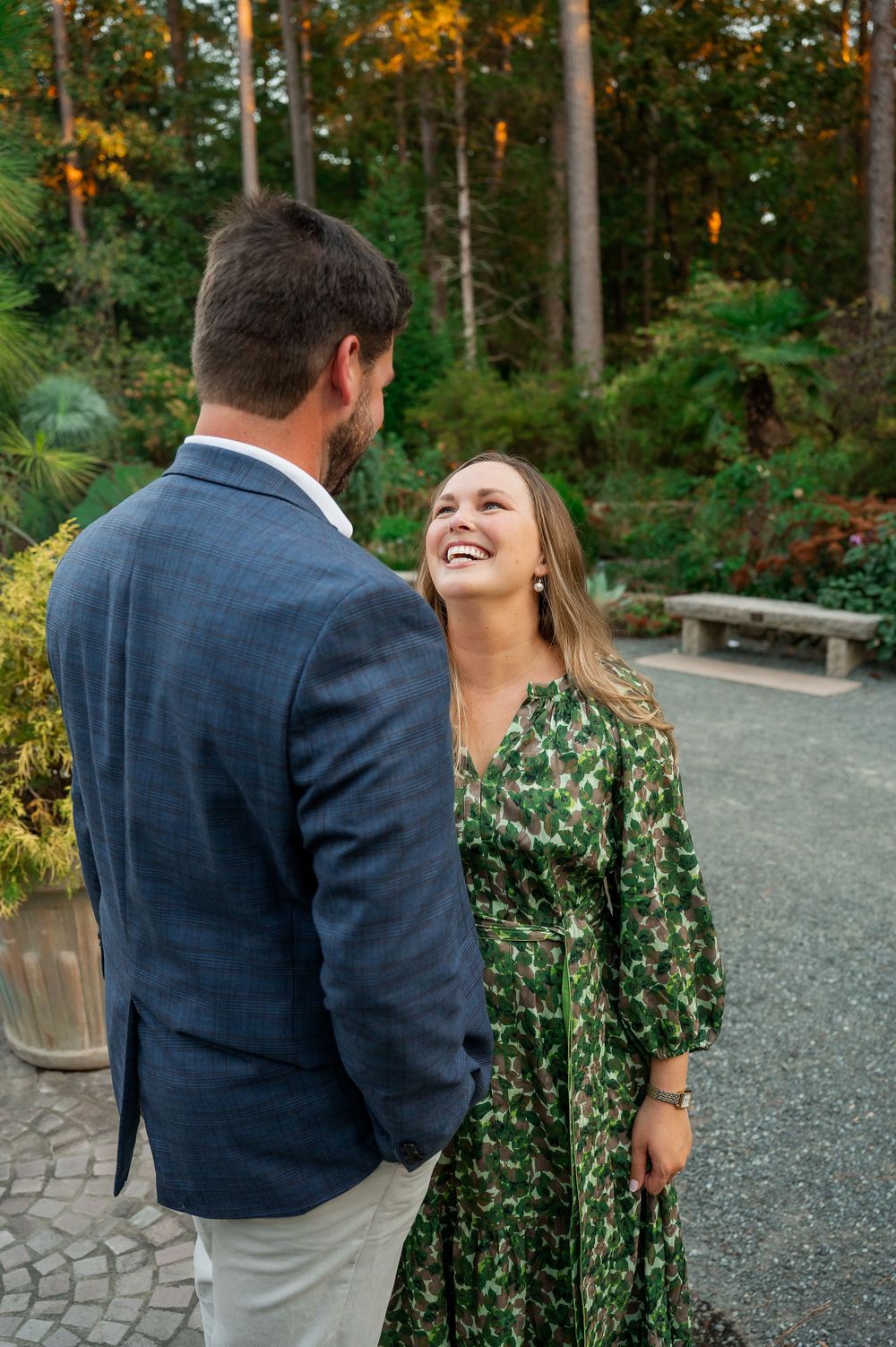 A couple laughing together on a gravel path surrounded by autumn foliage.