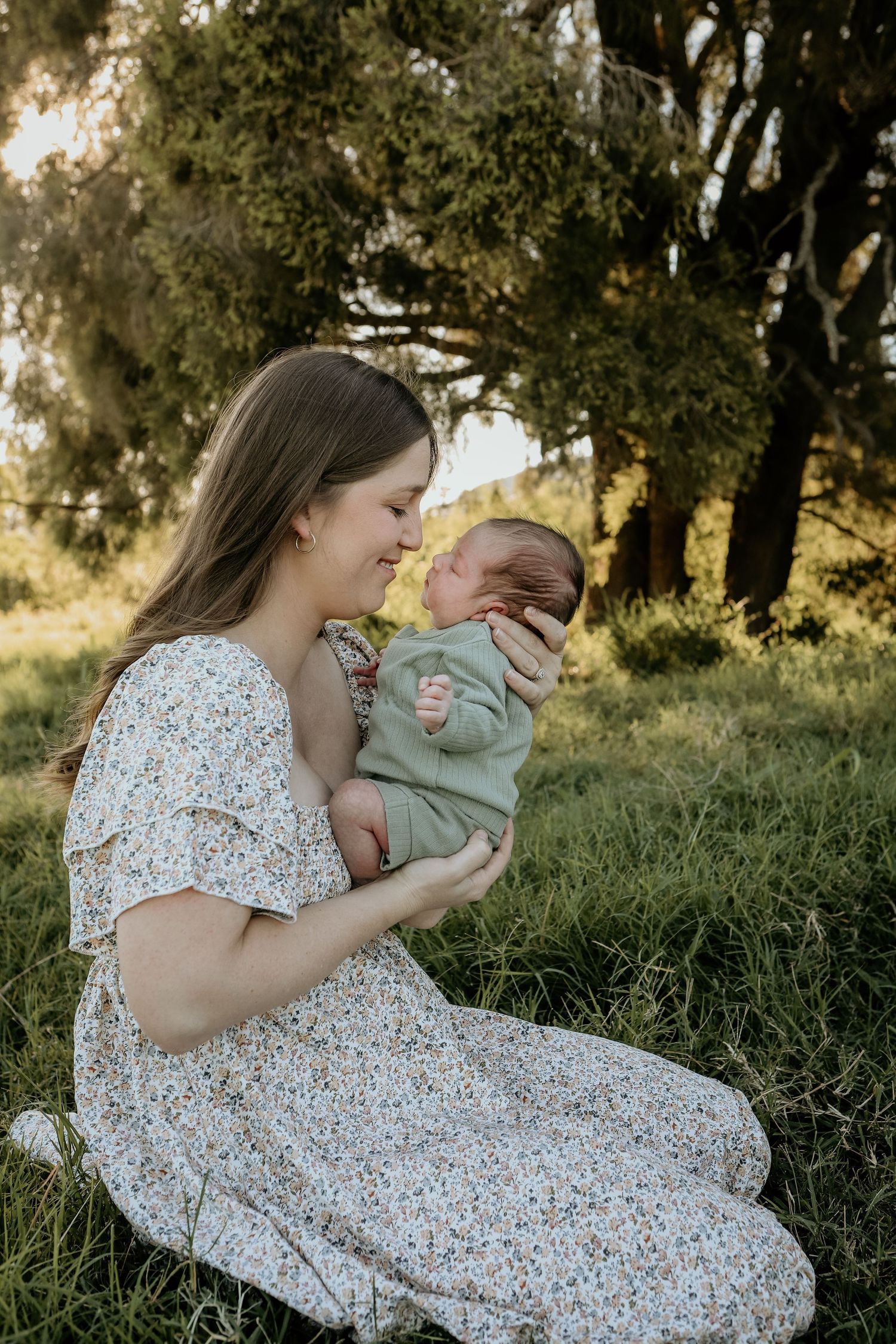 A tender moment captured in nature as parent and baby sit together on grassy ground at sunset.