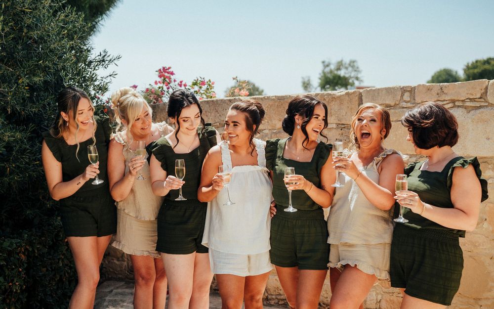 A group of bridesmaids in black and beige dresses pose together for wedding photos outdoors.