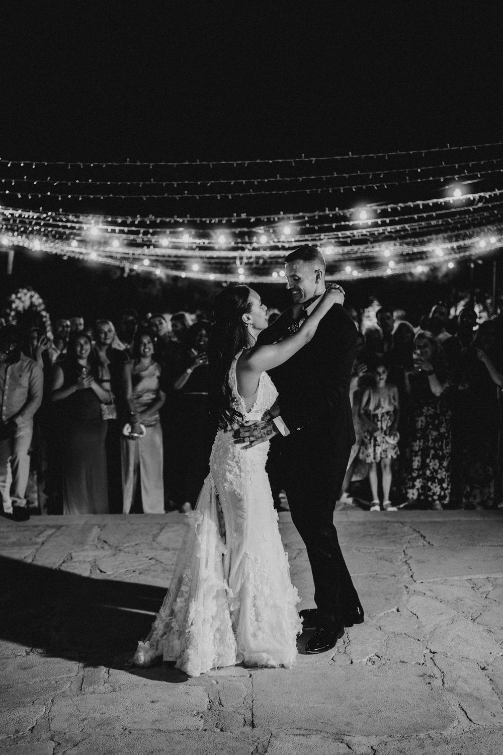 Black and white photos capture couples dancing under string lights at an outdoor wedding reception on stone patio.