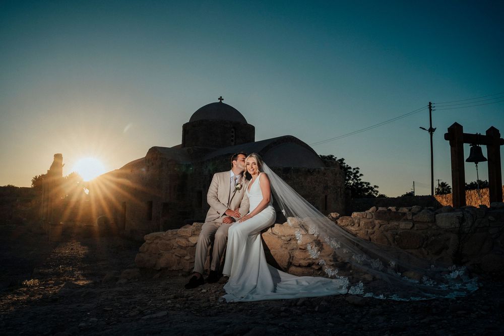 Silhouetted couple in wedding attire embraces against dramatic sunset sky at scenic mountain overlook.