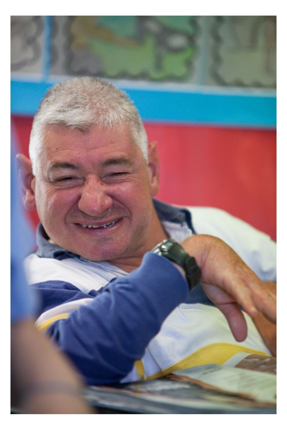 A person wearing a blue and white outfit smiles warmly while resting on a surface with red and blue colors visible.