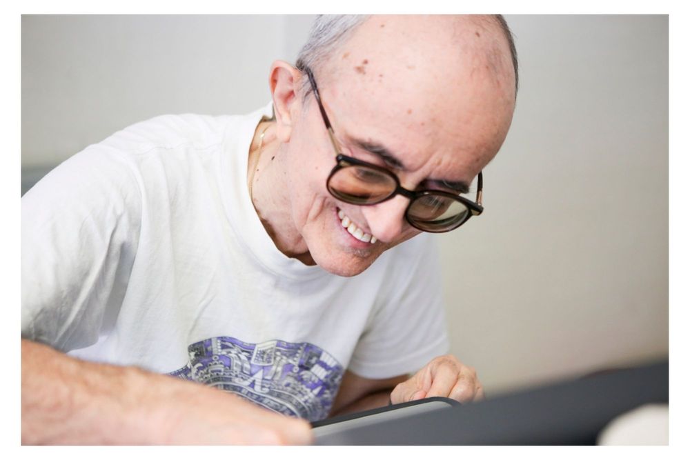 A person wearing glasses works intently on a laptop computer while sitting at a desk.