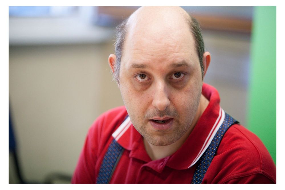 Person wearing a red shirt and overalls looking to the side in an indoor setting.