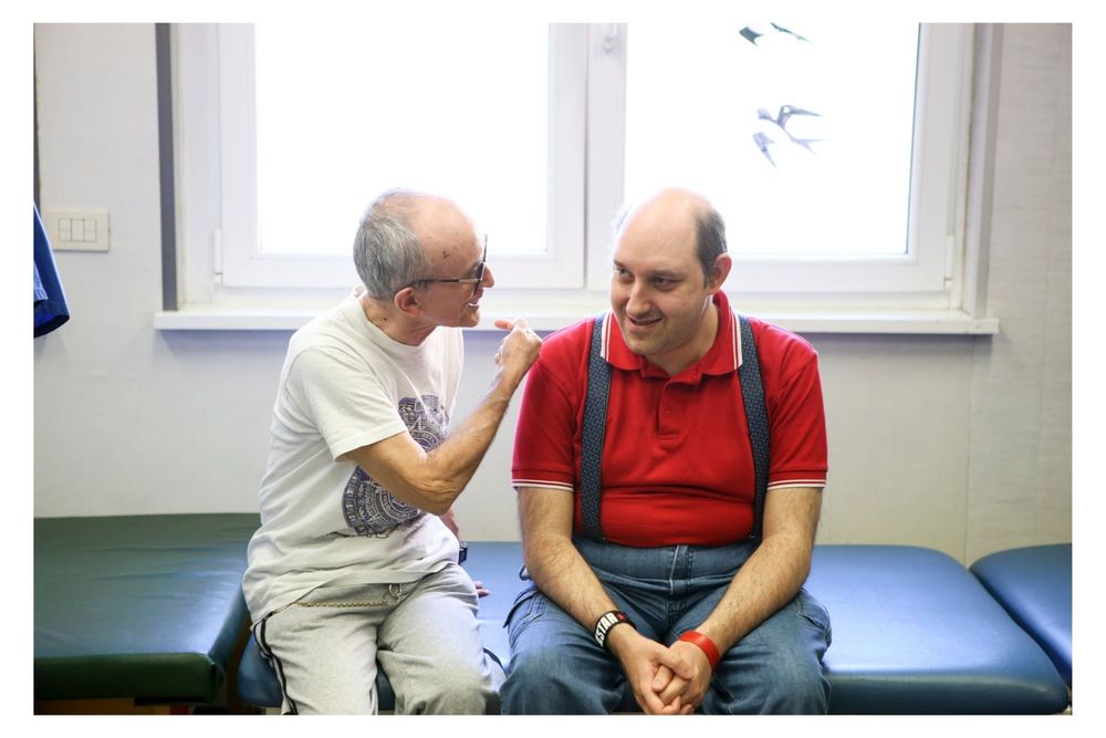 A medical professional in white consults with a patient wearing a red shirt while sitting on an exam table in a clinic.