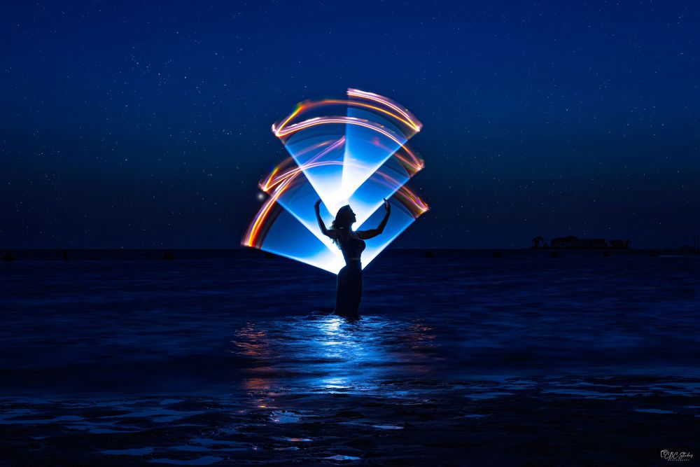 Light painting photography creates glowing circles over a dark ocean horizon at twilight.