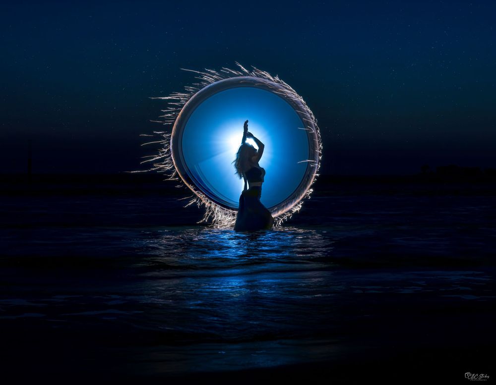 Artistic light trails form circular halos over water during blue hour photography.