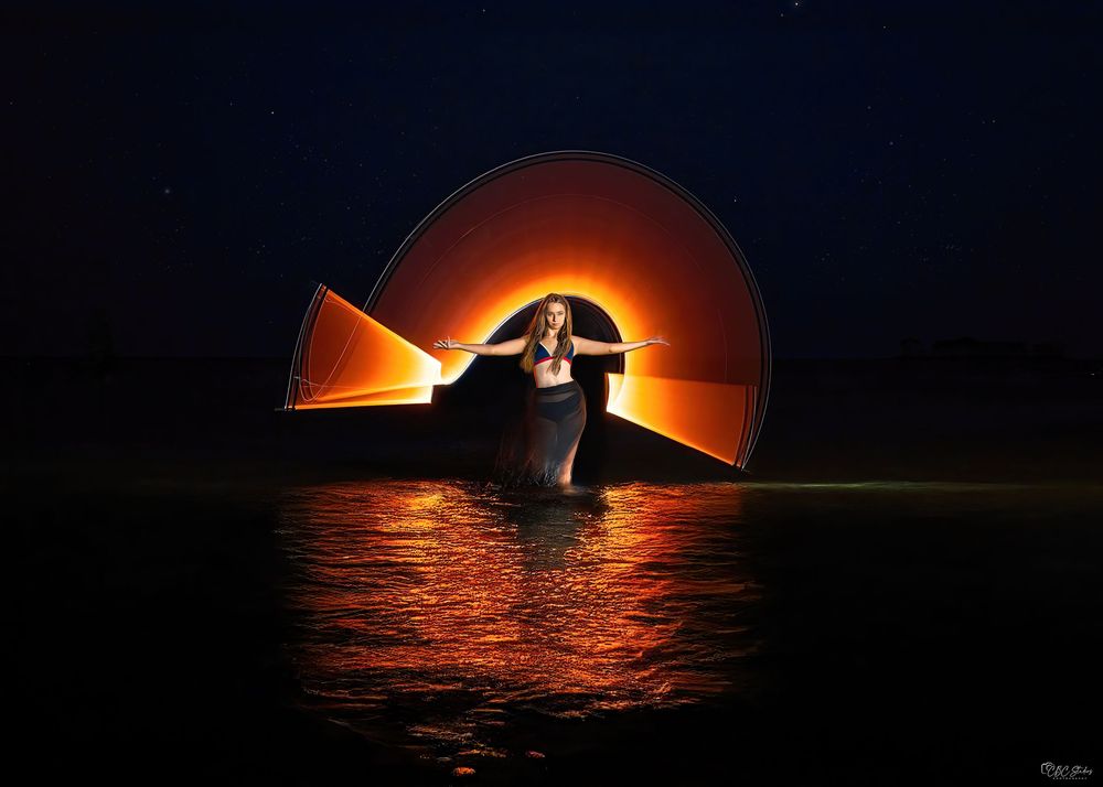 Silhouetted sailboat against vibrant orange sunset over calm ocean waters creates dramatic maritime scene.