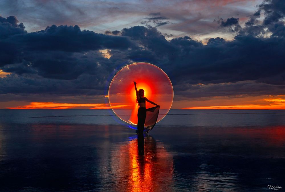 Silhouette of a cross against vibrant orange sunset over calm ocean waters creates dramatic spiritual scene.